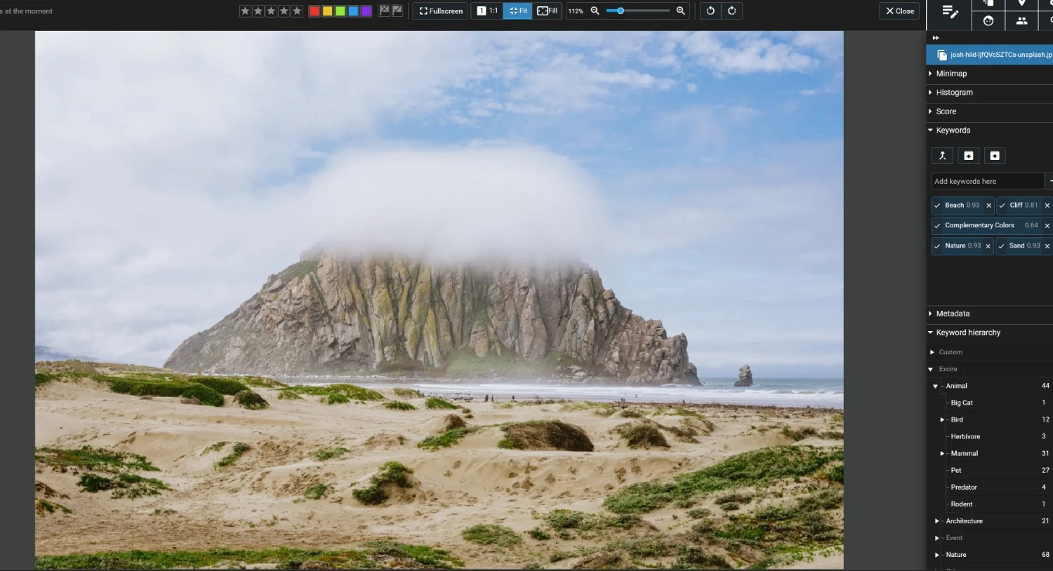 An image of a rock formation along a beach with low clouds displayed with keywords in Excire Foto 2024.