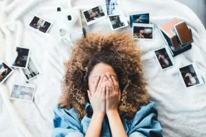Person sitting on a bed surrounded by photos struggling to get organized