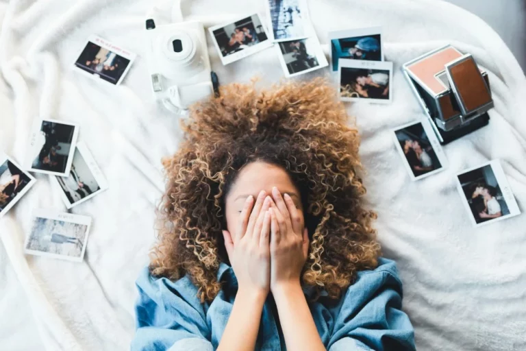 Person sitting on a bed surrounded by photos struggling to get organized