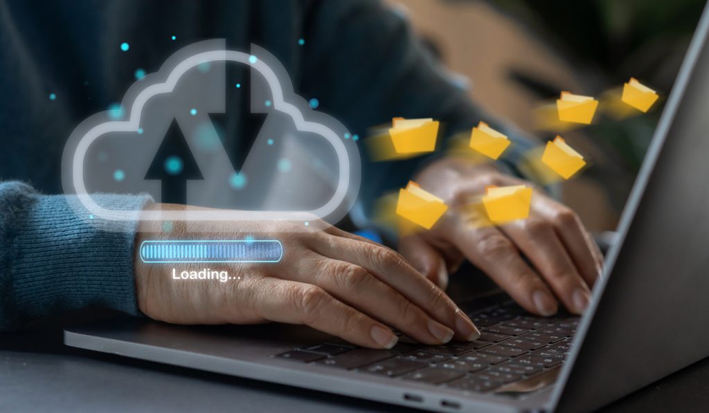 Hände tippen auf Laptop, während Dateien in die Cloud hochgeladen werden