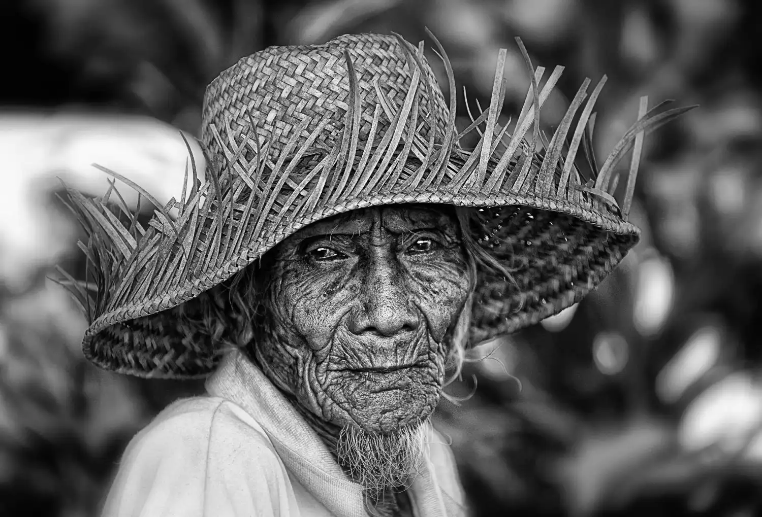 A black and white photo of an older man with a wrinkled face and a straw hat